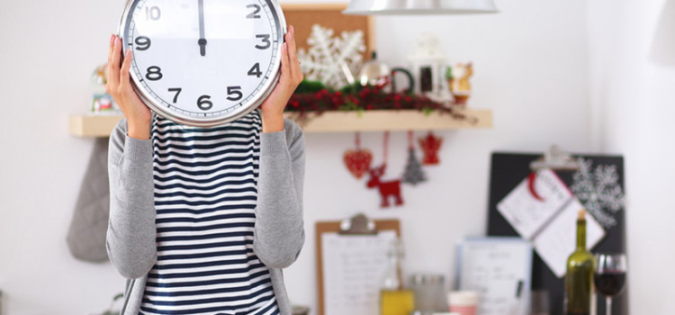 A woman standing in front of a kitchen area, holding a clock in front of her face