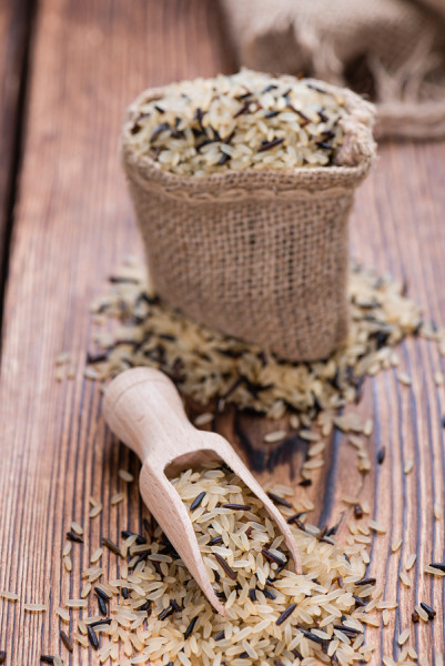 A small canvas bag filled to over flowing with mixed, uncooked rice grains.