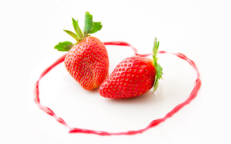 2 strawberries laying on a white surface, surrounded in a heart shaped line that has been drawn with strawberry juice