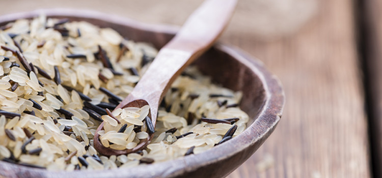 Mixed rice in a wooden bowl with a wooden spoon in it, all sitting on a rough wooden table top