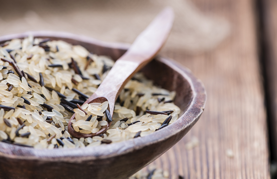 Mixed rice in a wooden bowl with a wooden spoon in it, all sitting on a rough wooden table top