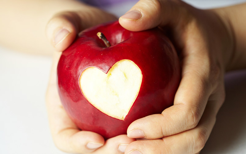 A childs hands holding an apple that has had a heart shaped bite taken out of it