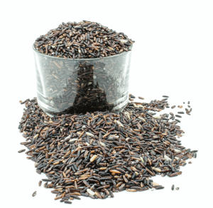 Brown rice grains in a glass bowl that is on a white tabletop. Rice has spilled in front of the bowl