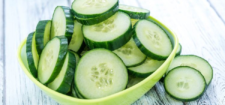 sliced cucumbers in a square green bowl on a wooden tabletop