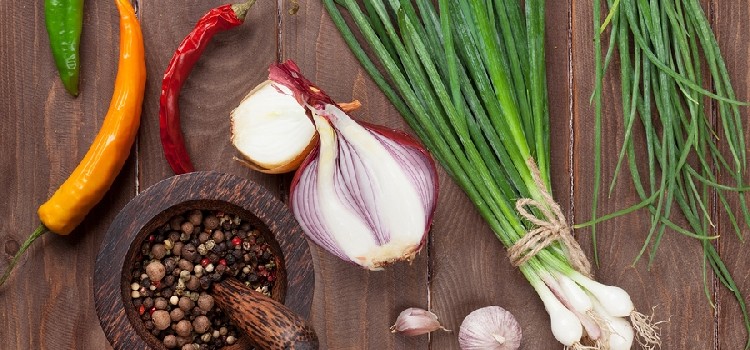 wooden table top with onions, peppers and other herbs and vegetables on it.