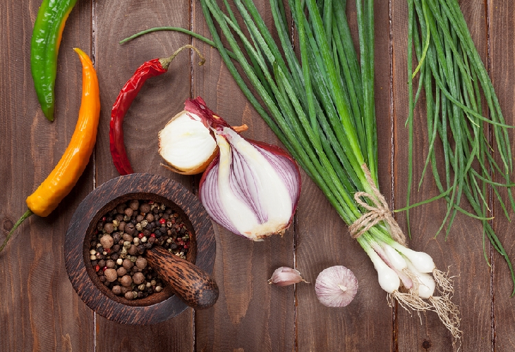 wooden table top with onions, peppers and other herbs and vegetables on it.