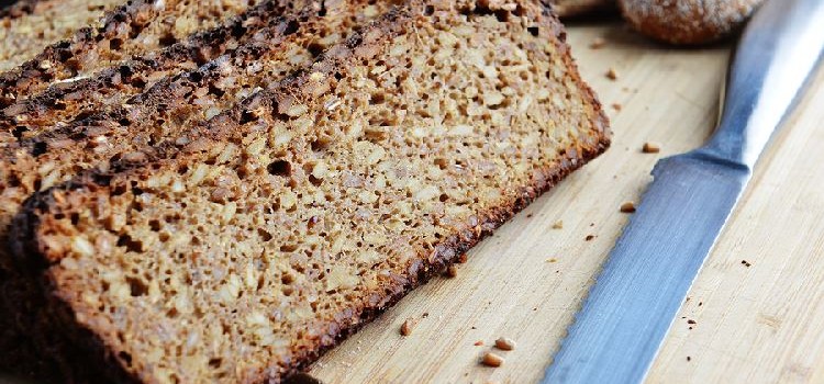 Slices of sprouted whole grain bread on a wooden cutting board with a bread knife in the foreground