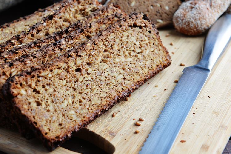 Slices of sprouted whole grain bread on a wooden cutting board with a bread knife in the foreground