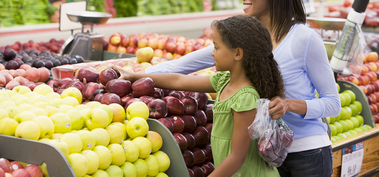 A woman and young girl shopping for fruit in a grocery store