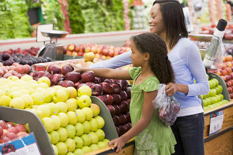 A woman and young girl shopping for fruit in a grocery store